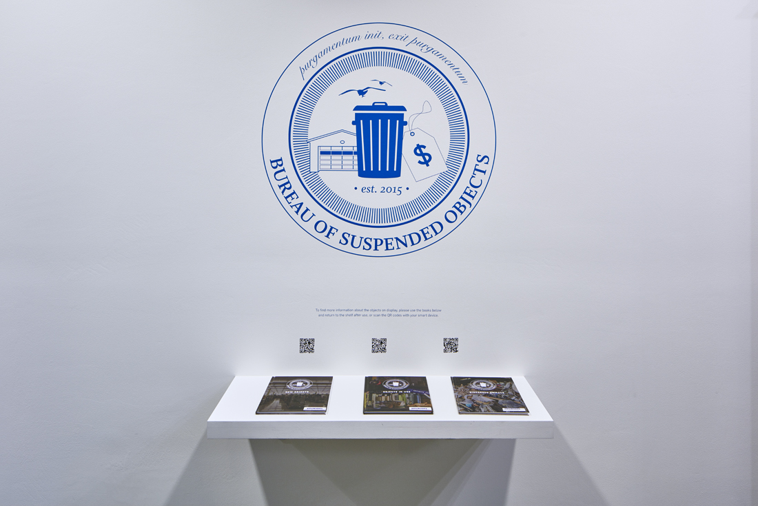 Below a large logo for the Bureau of Suspended Objects, a shelf containing three books, one for each section of the display case