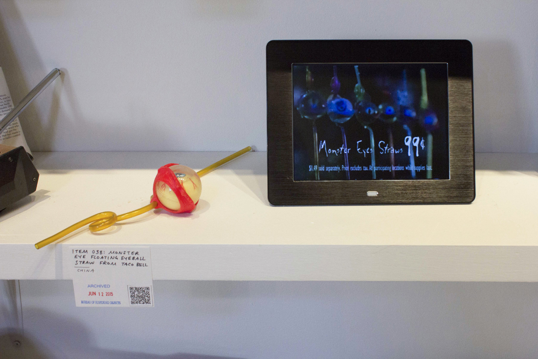A twisted plastic straw with attached floating toy eyeball next to a digital photo frame playing the original Taco Bell commercial, in which the straws were 99 cents with a meal