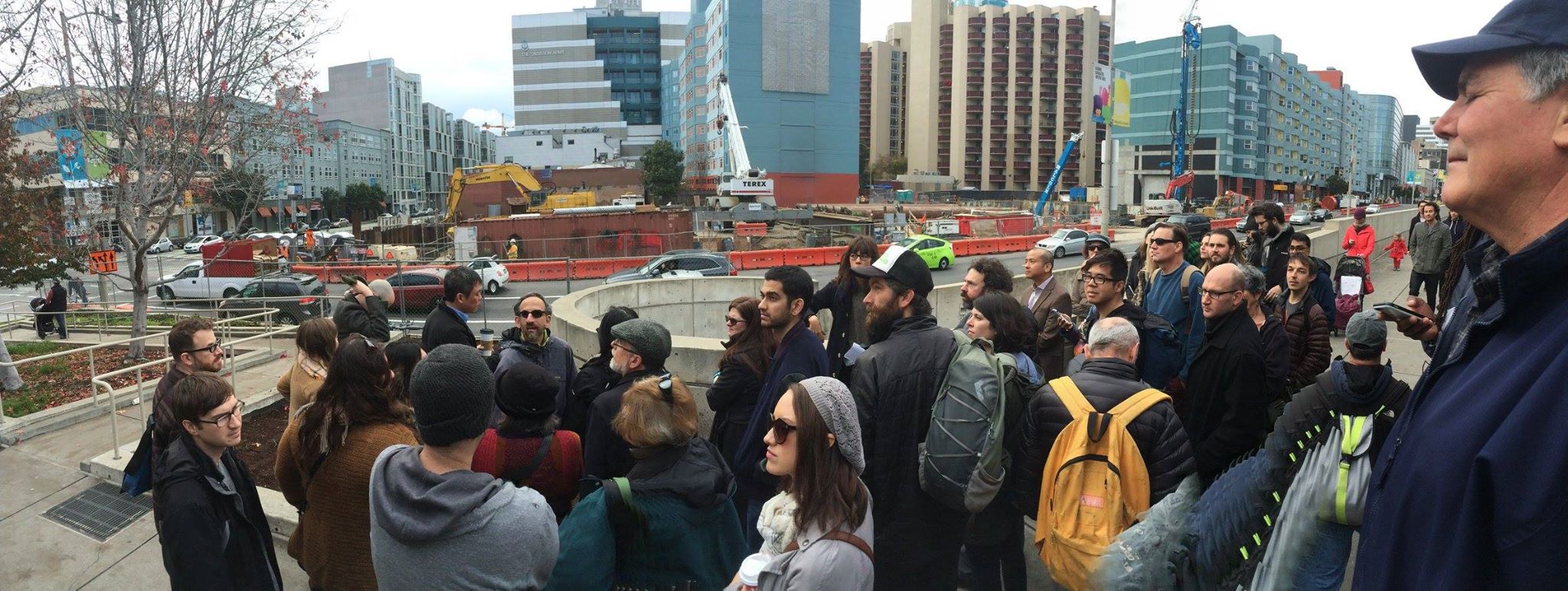 a panoramic photo of a crowd standing near a construction site in the SOMA neighborhood, with me in the background pointing and talking